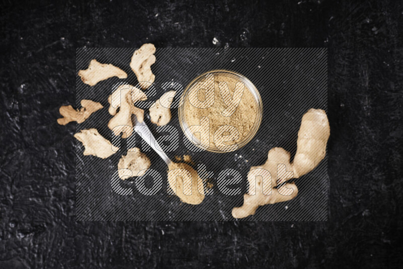 A glass jar full of ground ginger powder on black background