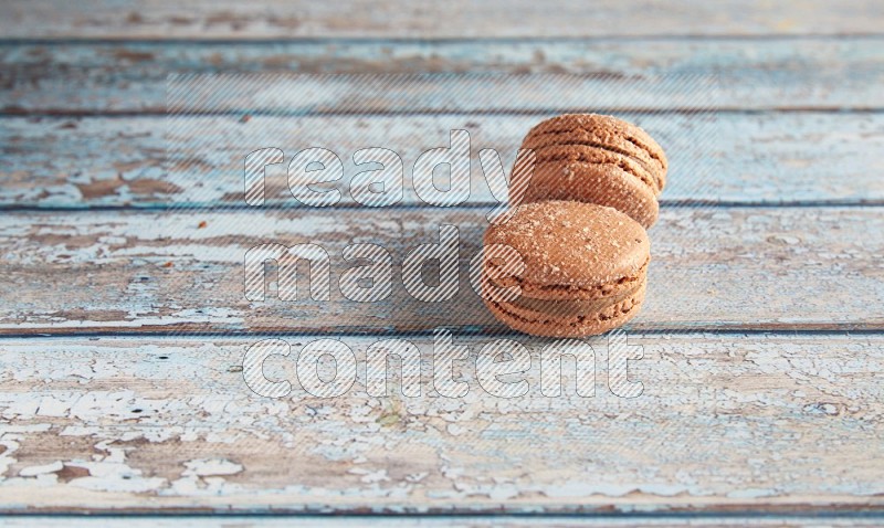 45º Shot of two Brown Hazelnuts macarons on light blue wooden background