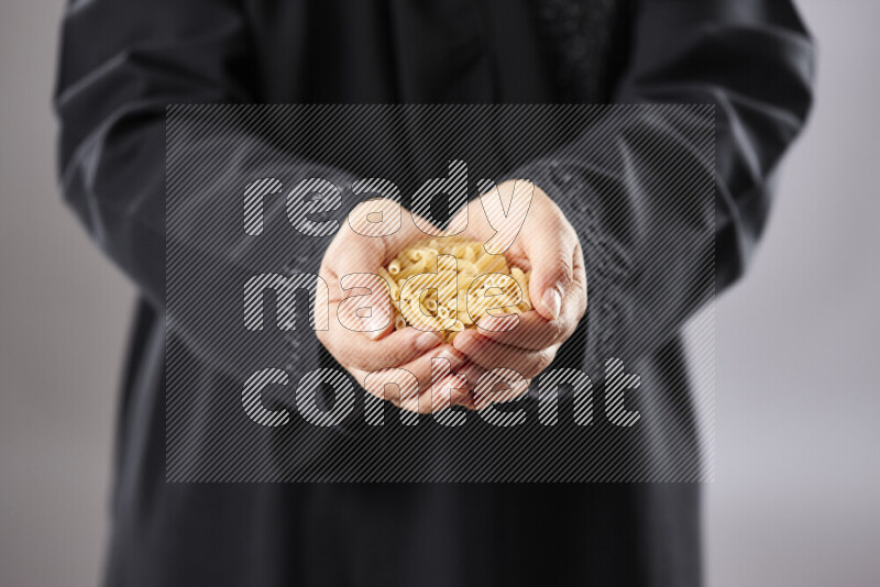 Woman in abaya holding different kinds of pasta in different positions