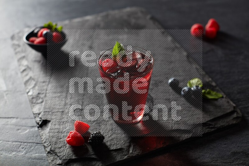 A glass of mixed berries juice with mint leaves on black background