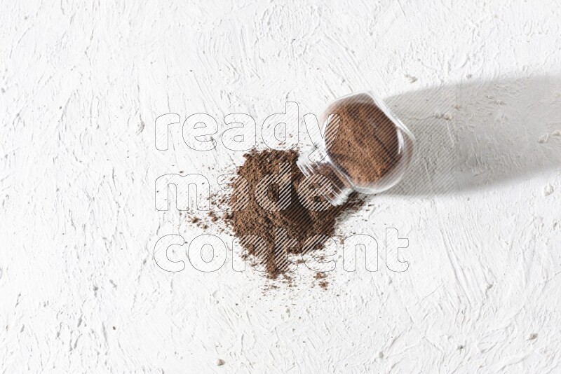 وعاء زجاجي مقلوب ممتلئ ببودرة القرنفل وتناثرت البودرة منه على أرضية بيضاء