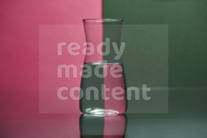 The image features a clear glassware filled with water, set against pink and dark green background