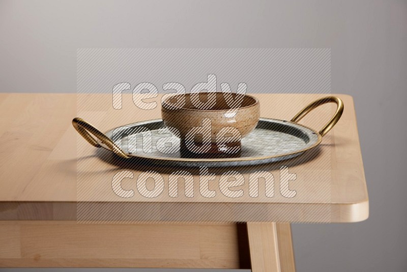 multicolored bowl placed on a rounded stainless steel tray with golden handels on the edge of wooden table