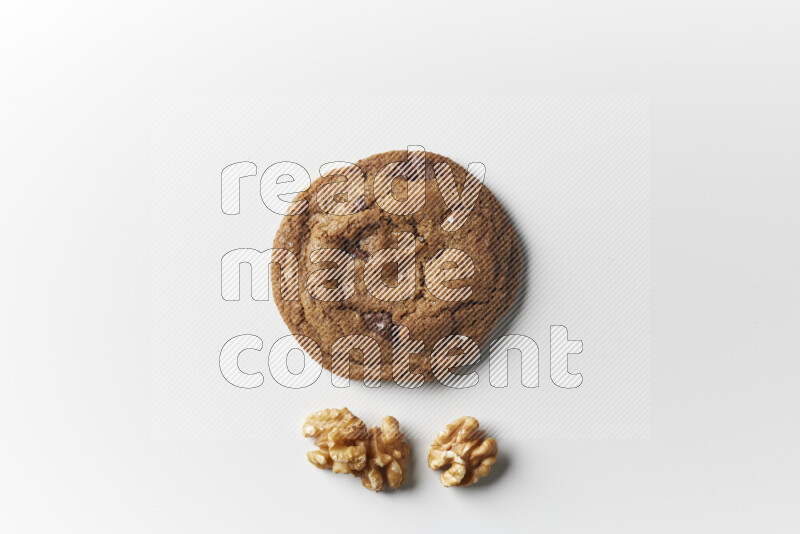 A single chocolate chips cookie with walnuts beside it on a white background