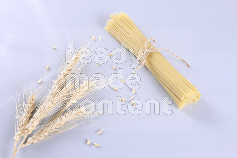 Raw pasta with wheat stalks on light blue background