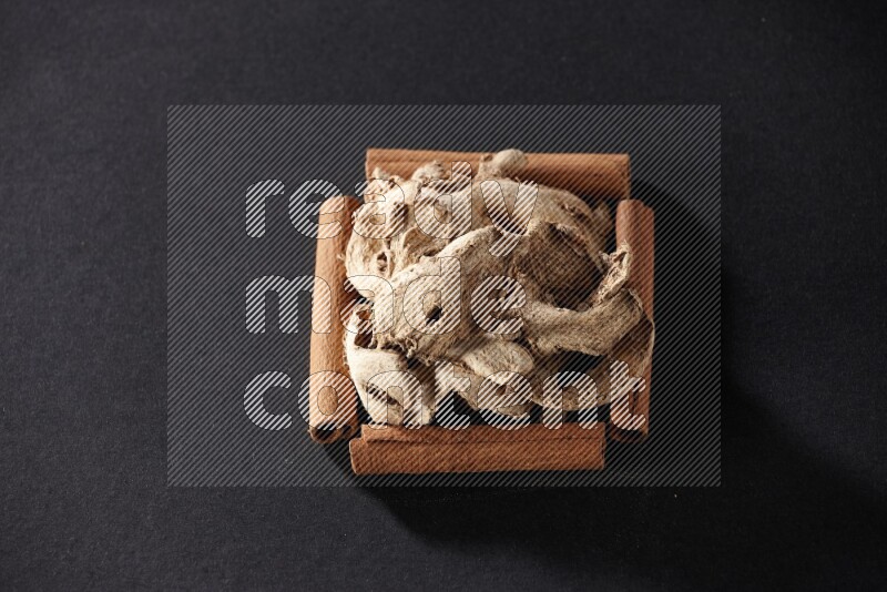 A single square of cinnamon sticks full of dried ginger on black flooring