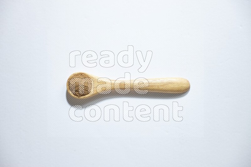 A wooden spoon full of cumin powder on a white flooring