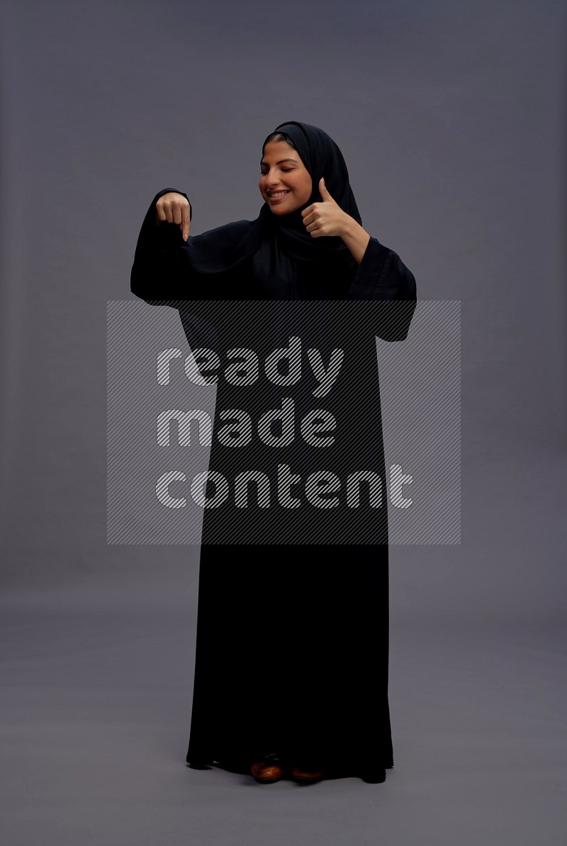 Saudi woman wearing Abaya standing interacting with the camera on gray background