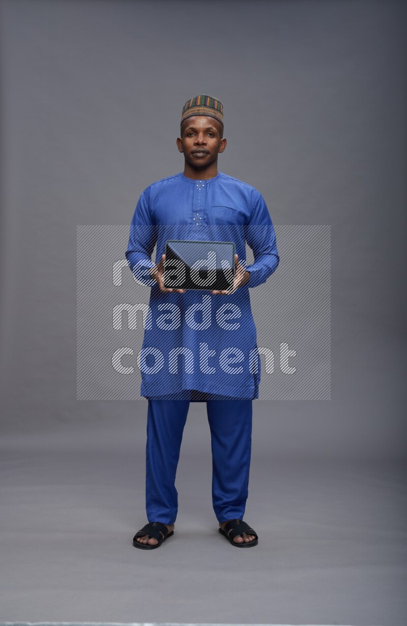 Man wearing Nigerian outfit standing showing tablet to camera on gray background
