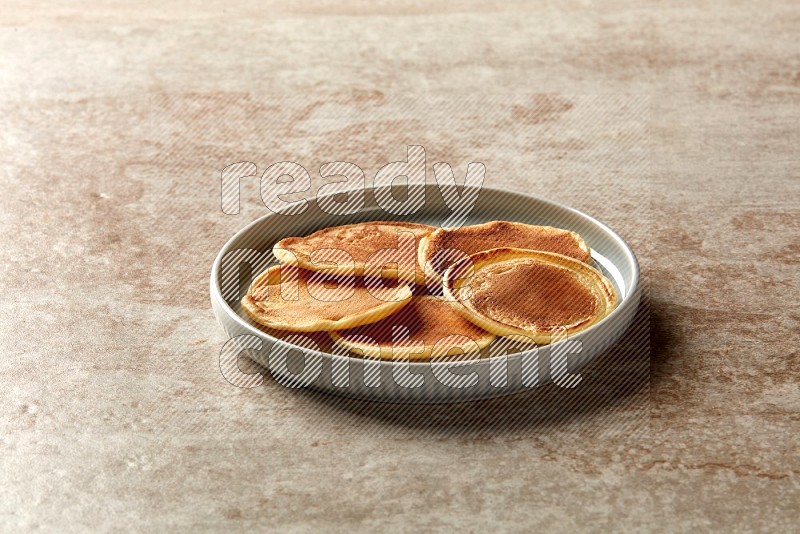 Five stacked plain mini pancakes in a blue plate on beige background