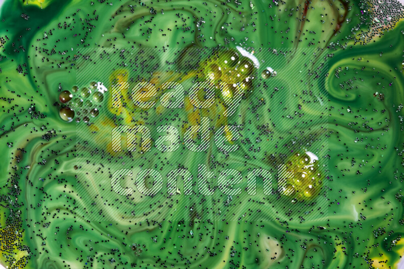 A close-up of sparkling green glitter scattered on swirling yellow and green background
