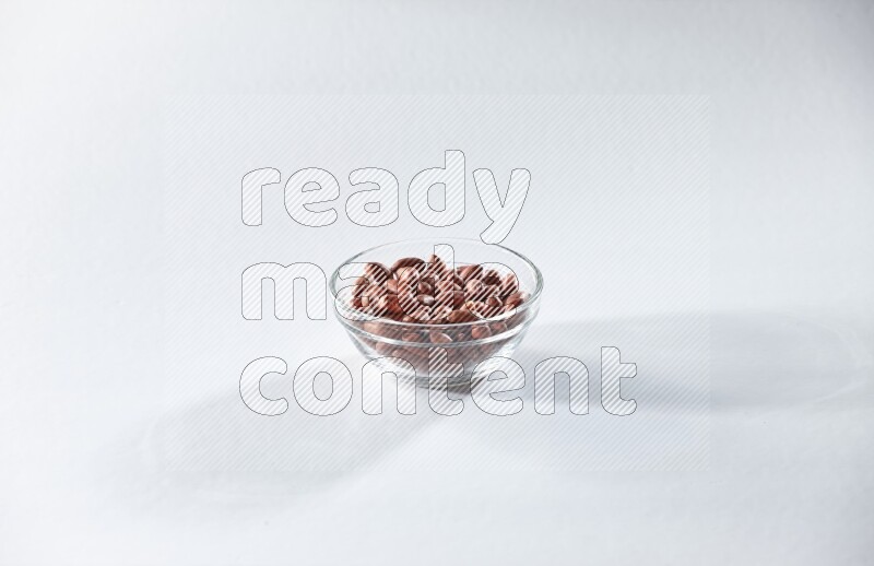 A glass bowl full of red skin peanuts on a white background in different angles