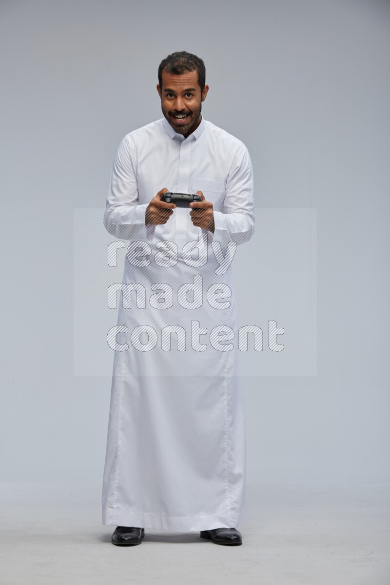 Saudi man Wearing thob standing holding joystick on Gray background
