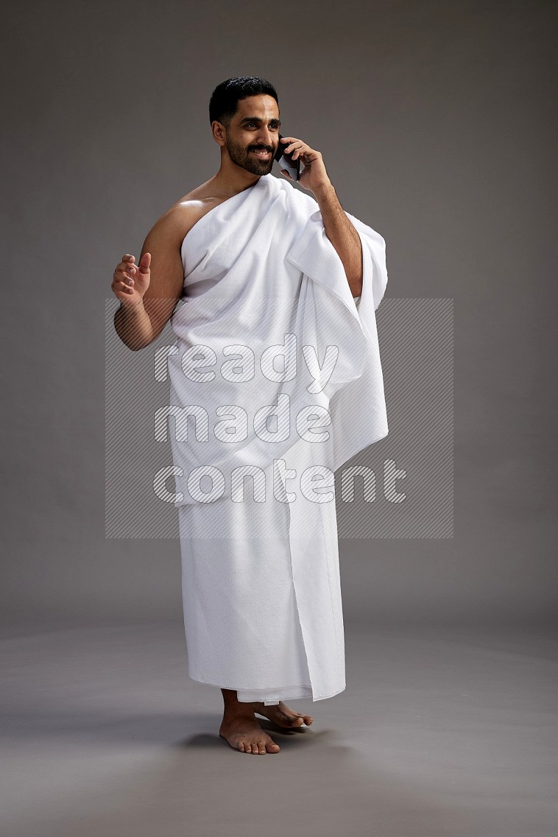 A man wearing Ehram Standing talking on phone on gray background