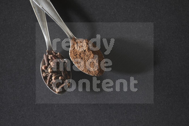 ملعقتان معدنيتان، إحداهما ممتلئة بحبوب القرنفل والأخرى ببودرة القرنفل، على خلفية سوداء