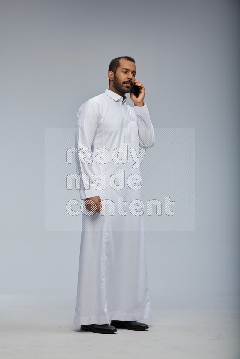 Saudi man wearing Thob standing talking on phone on Gray background