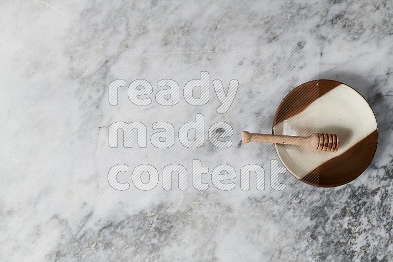 Multicolored Pottery Plate with wooden honey handle in it, on grey marble flooring, Top View