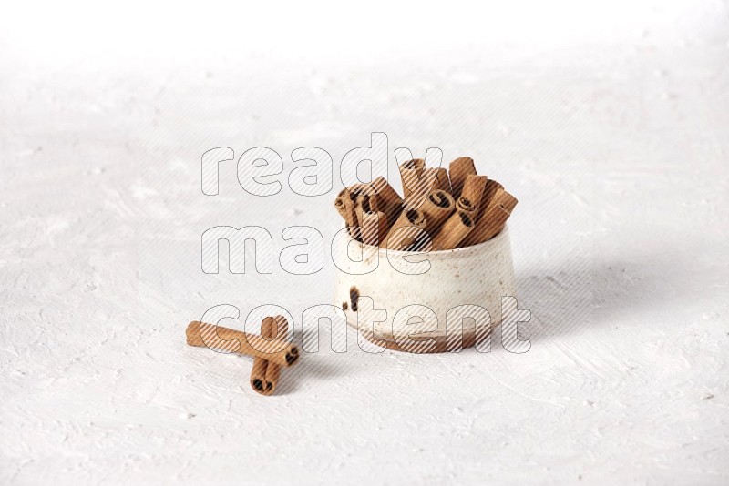 Cinnamon sticks in a beige bowl on a white background