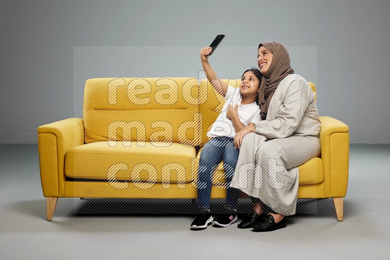 A girl sitting taking selfie with her mother on gray background