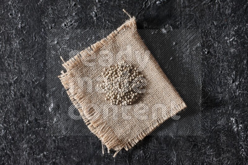 White pepper beads on a burlap piece of fabric on textured black flooring