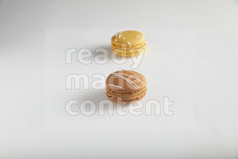 45º Shot of of two assorted Brown Irish Cream, and Yellow Piña Colada macarons on white background