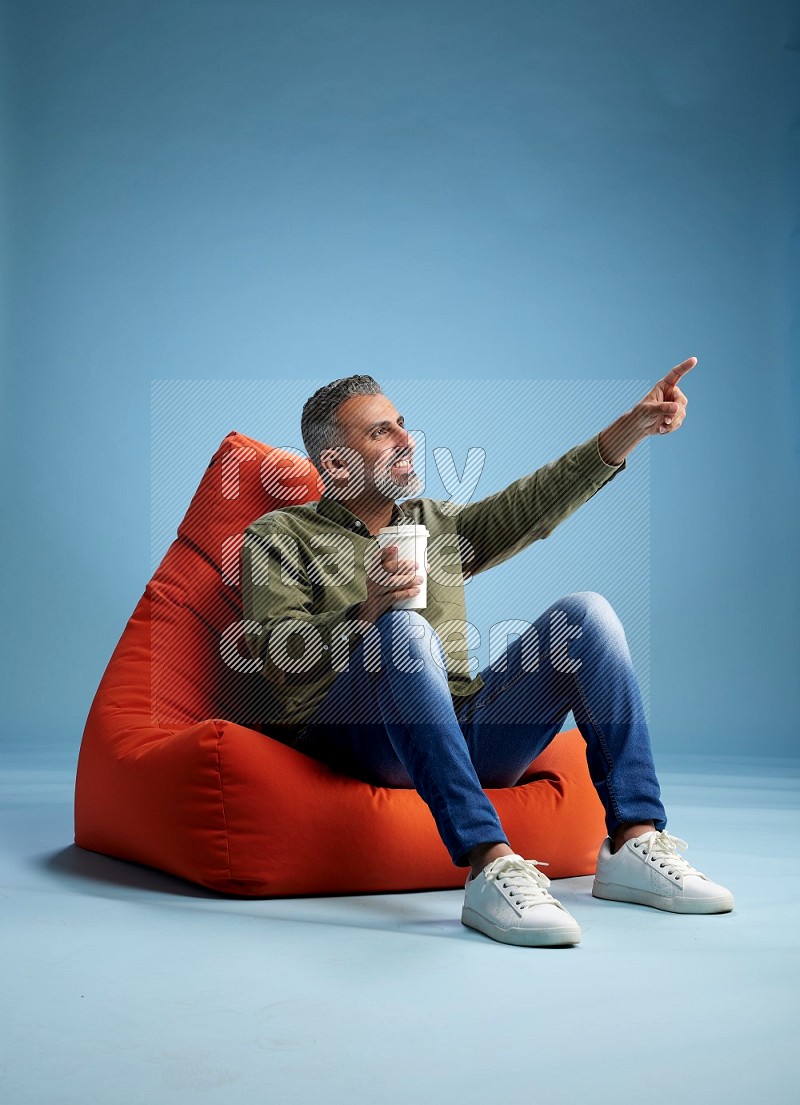 A man sitting on an orange beanbag and drinking coffee