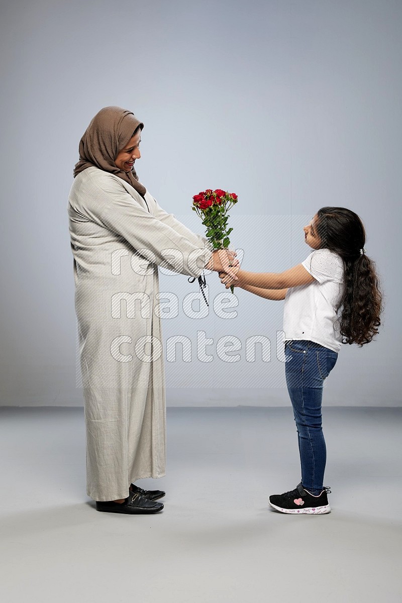 A girl standing giving flowers to her mother on gray background
