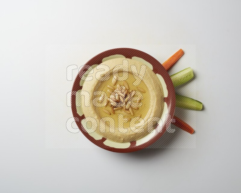 Hummus in a traditional plate garnished with pine nuts on a white background