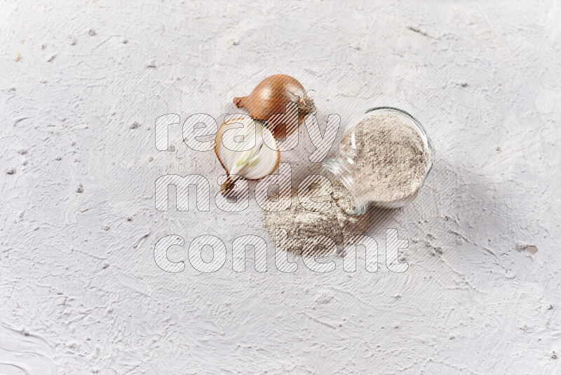 A glass jar full of onion powder flipped with some spilling powder on white background