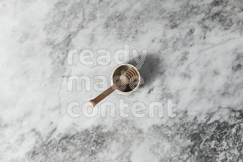 Black Pottery Bowl with wooden honey handle in it, on grey marble flooring, Top View
