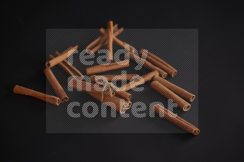 4 Cinnamon sticks stacked and bounded with more sticks in the background on black flooring
