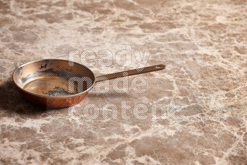 A small copper pan on beige marble background