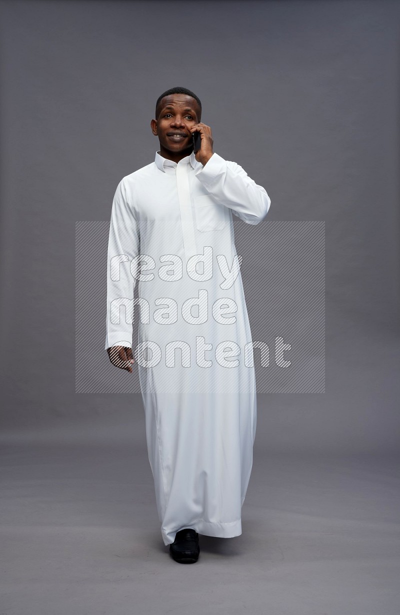 Saudi man wearing thob standing talking on phone on gray background