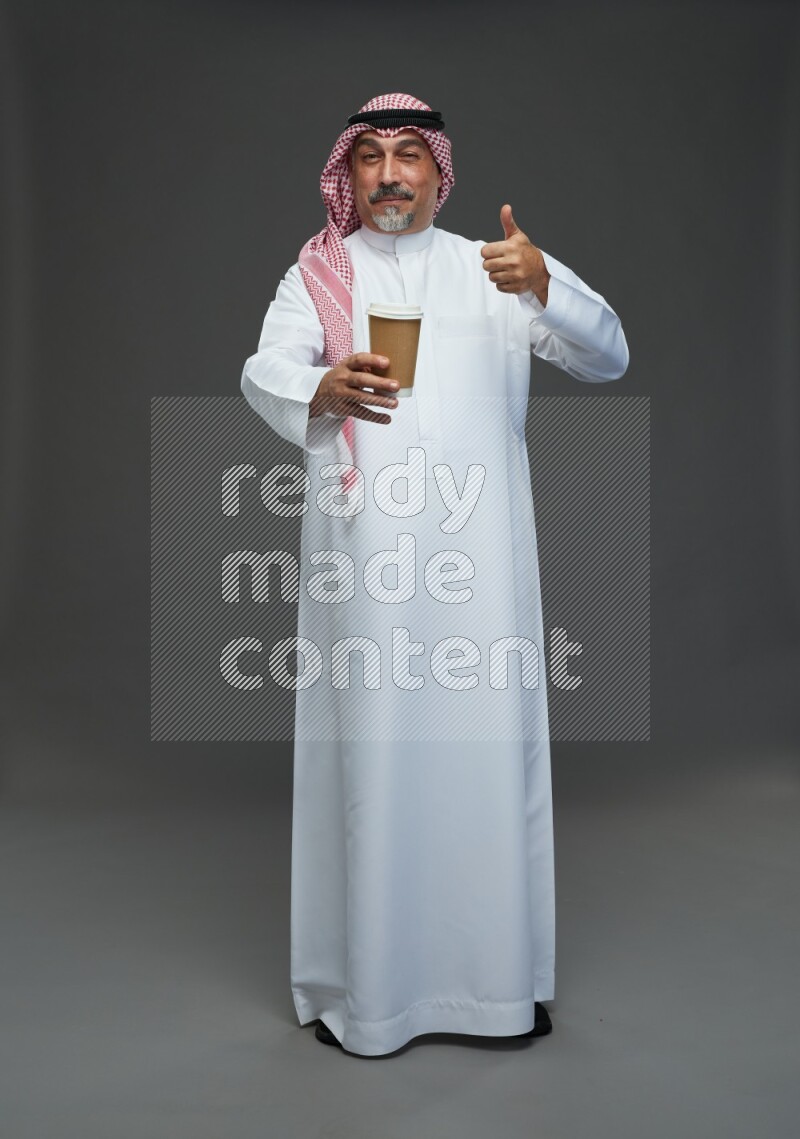 Saudi man with shomag Standing holding paper cup on gray background