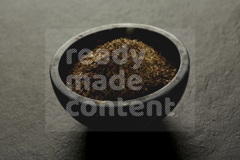 black pottery round sauce bowl filled with herbs on grey textured countertop