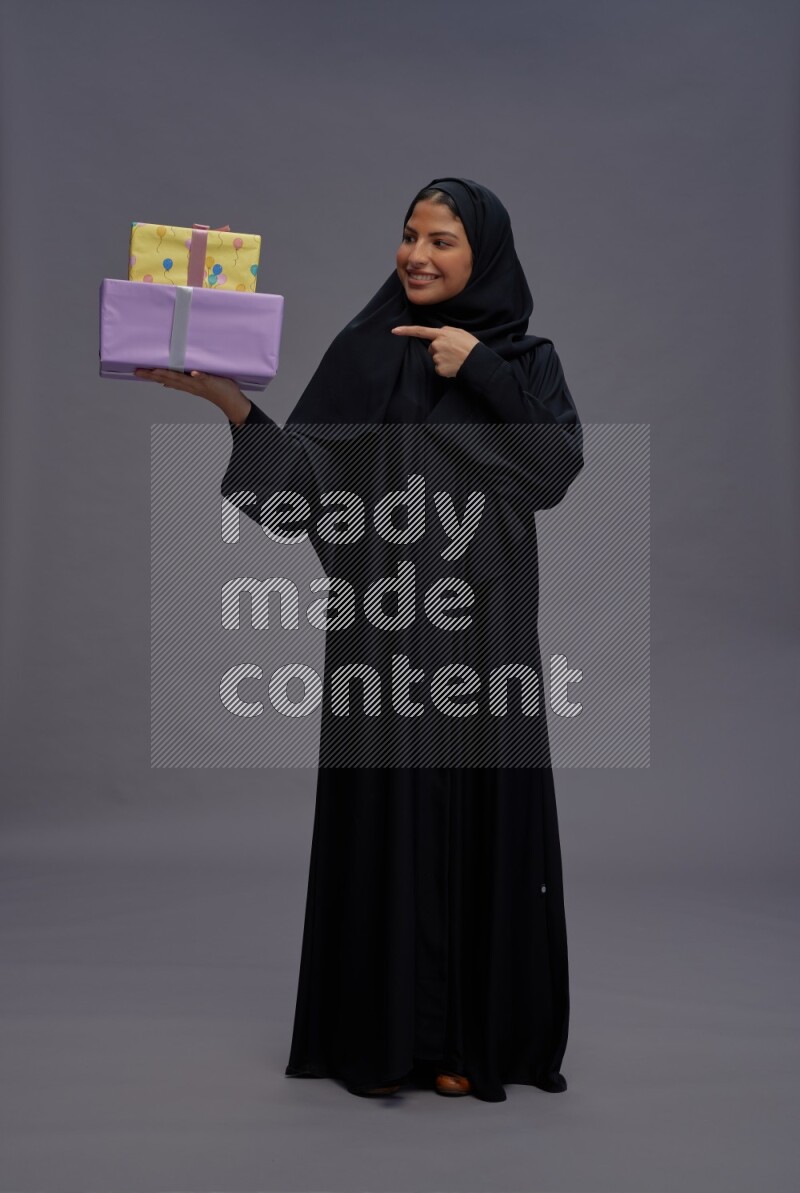 Saudi woman wearing Abaya standing holding gift box on gray background