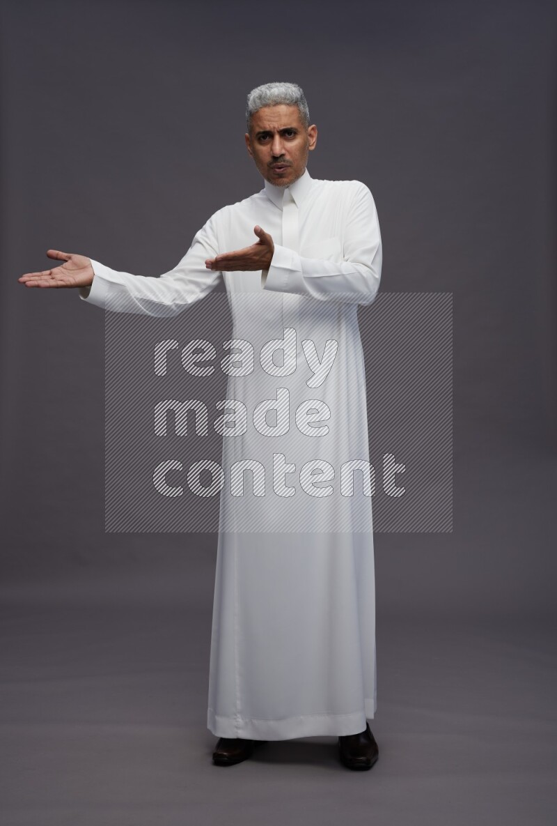 Saudi man wearing thob standing interacting with the camera on gray background