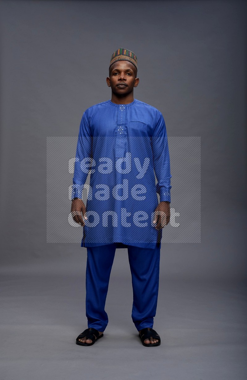 Man wearing Nigerian outfit standing interacting with the camera on gray background