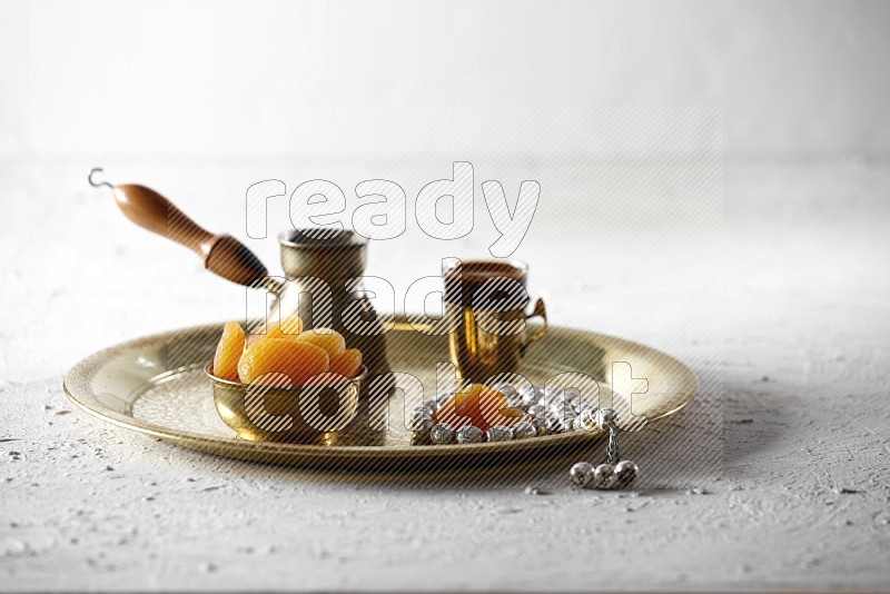 مشمش مجفف في وعاء معدني مع القهوة وسبحة على صينية علي خلفية بيضاء