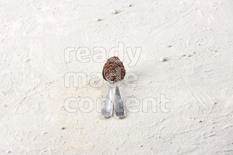 ملعقتان معدنيتان ممتلئتان بحبوب بذر الكتان على أرضية بيضاء