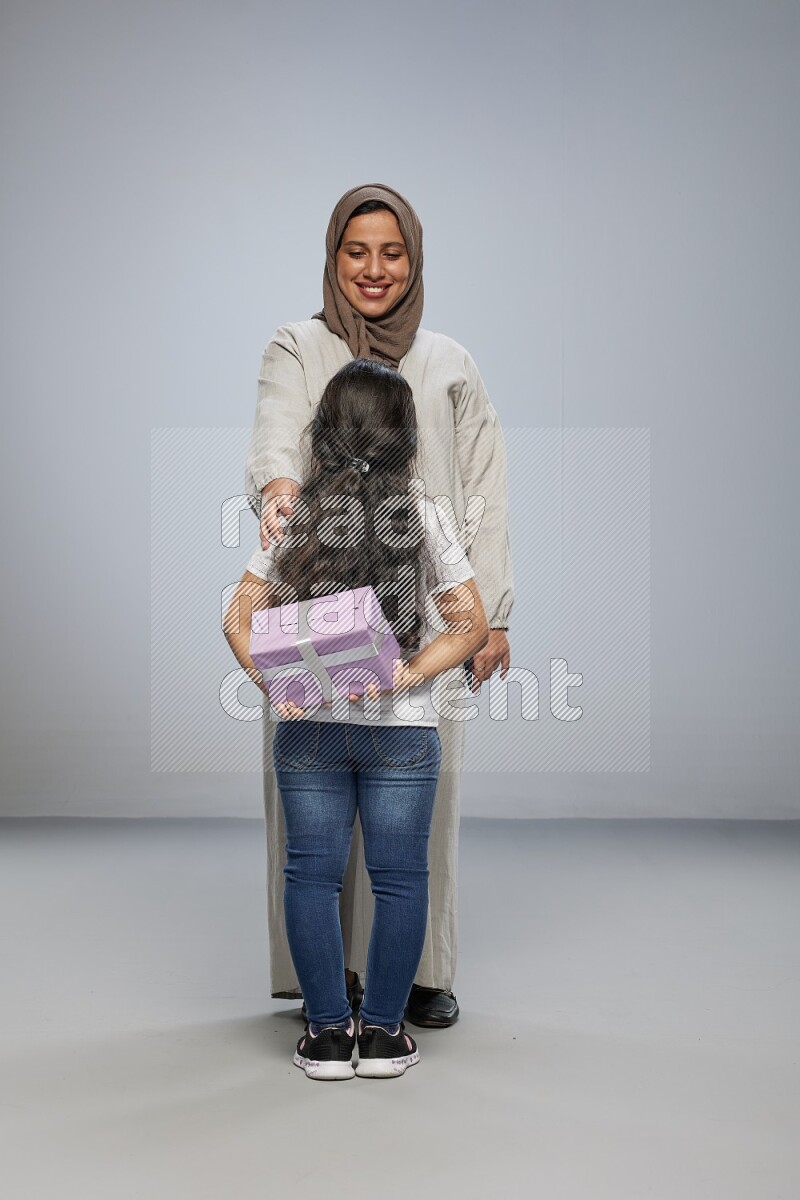 A girl standing hiding a gift behind her back for her mother on gray background