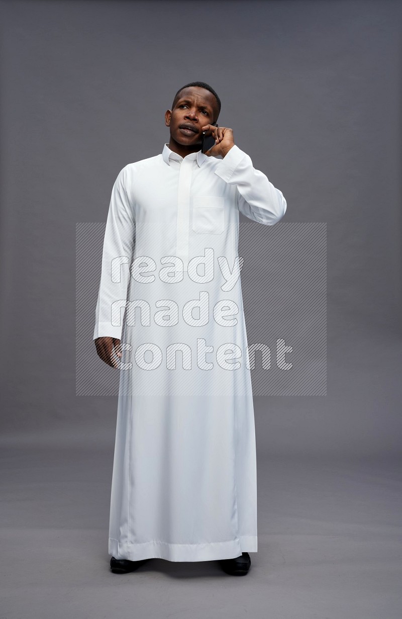 Saudi man wearing thob standing talking on phone on gray background