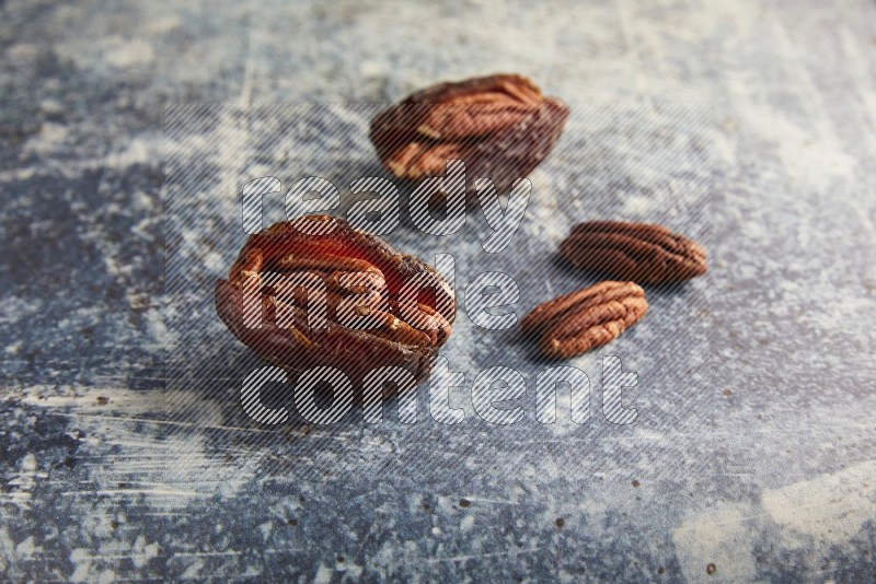 two pecan stuffed madjoul dates on a rustic blue background