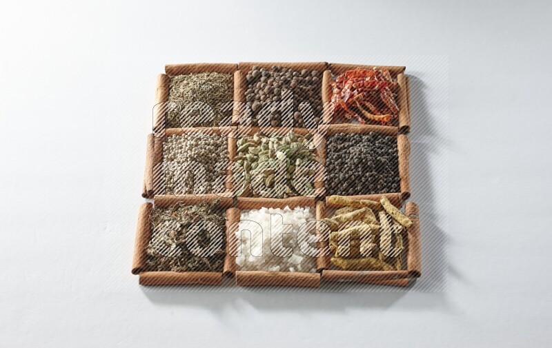 9 squares of cinnamon sticks full of cardamom in the middle surrounded by turmeric, salt, dried basil, white pepper, cumin, allspice, red dried chilis and black pepper on white flooring