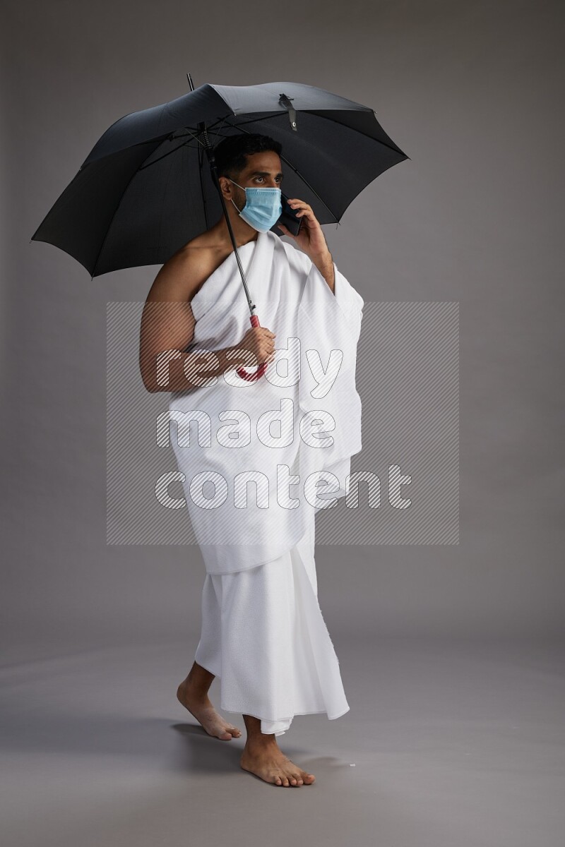 A man wearing Ehram and mask Standing holding umbrella on gray background on gray background