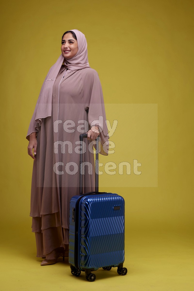 A woman With suit Case on a Yellow Background wearing Brown Abaya with Hijab