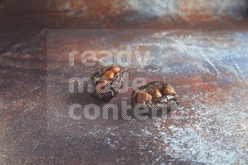 two hazelnut stuffed madjoul dates on a rustic reddish background