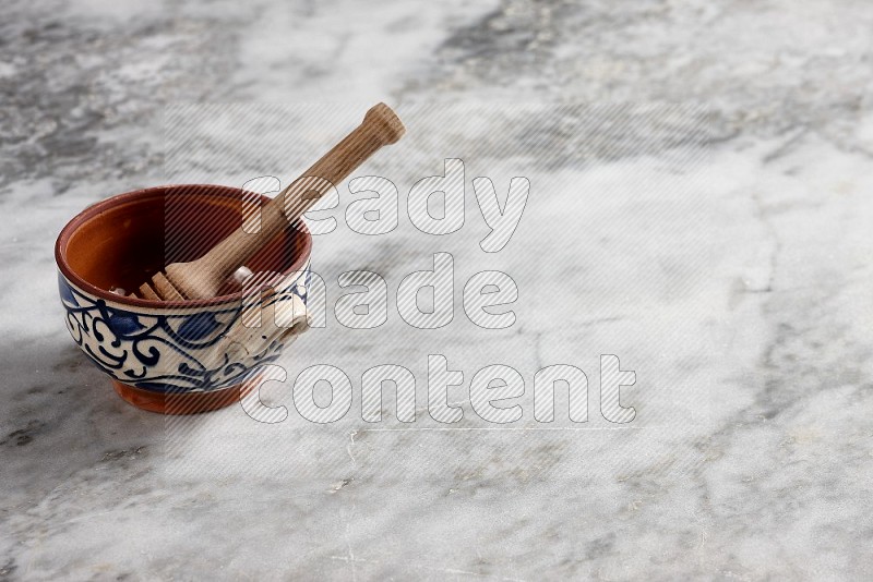 Decorative Pottery Pot with wooden honey handle in it, on grey marble flooring, 45 degree angle