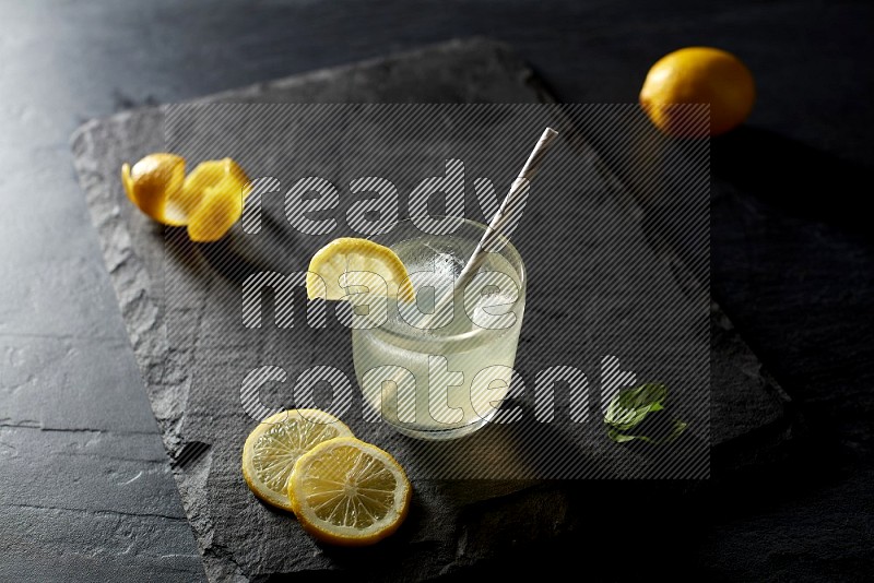 A glass of lemon juice with a straw on black background