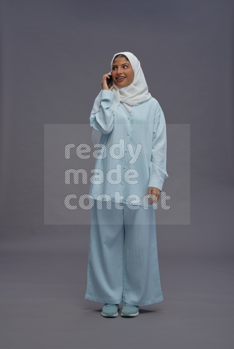 Saudi woman wearing hijab clothes standing talking on phone on gray background